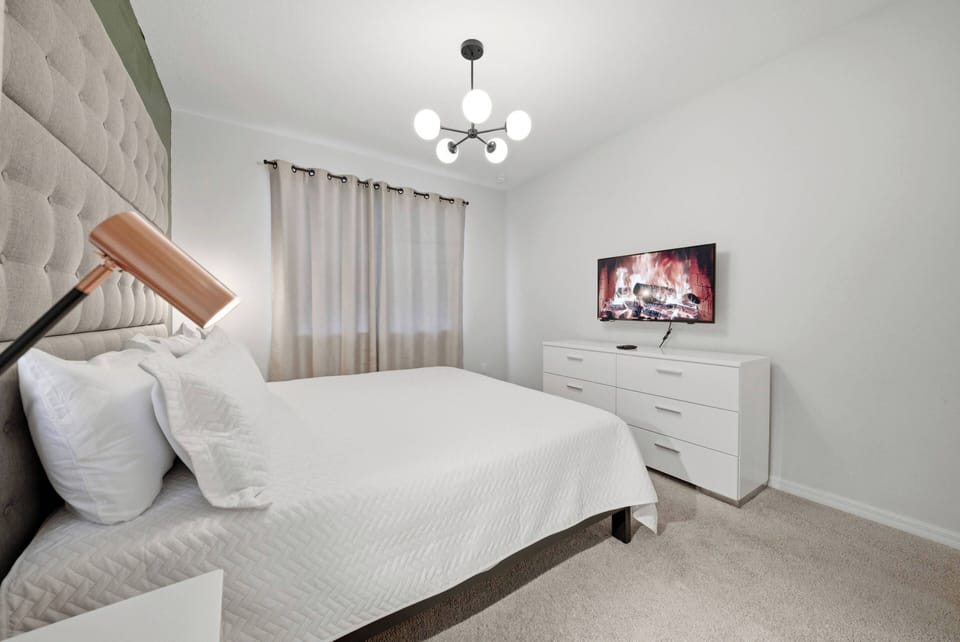 Experience a restful night in this thoughtfully designed bedroom, featuring a plush bed with a chic tufted headboard and soft, neutral tones. The stylish light fixture and modern TV add a touch of comfort, enhancing your stay.