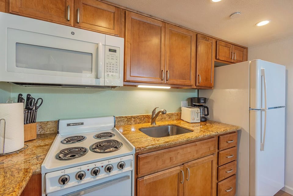 Your fully equipped kitchen features warm wood cabinetry and all the essentials—microwave, stove, refrigerator, and coffee maker—ready for preparing home-cooked meals.