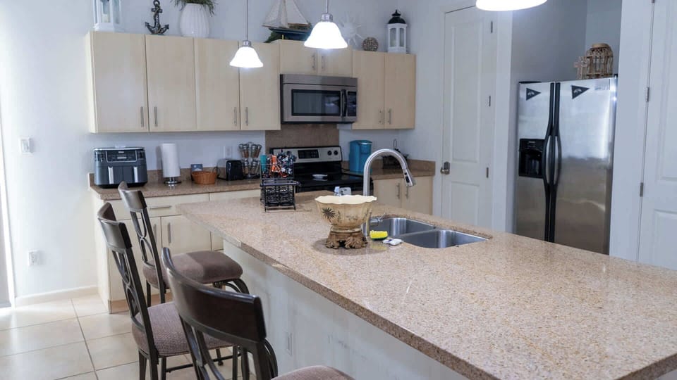 Coastal Kitchen with Bar Seating
Bright, fully equipped kitchen boasts granite counters, stainless appliances, and nautical decor. Perch on bar stools for casual meals amid wood cabinets and pendant lights—cook up beach day feasts effortlessly!