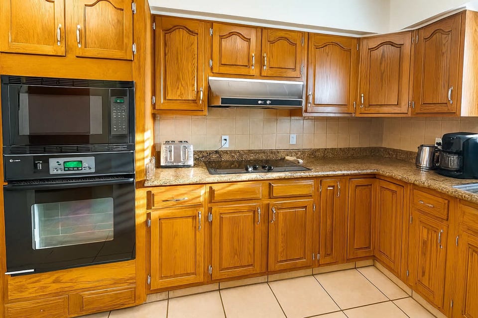 Modern kitchen with plenty of storage, granite countertops, and wooden cabinetry. Enjoy cooking with a built-in oven, microwave, stove, toaster, coffee maker, and kettle. Spacious layout makes preparing meals easy and enjoyable for guests.