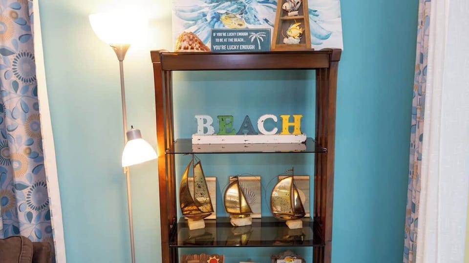 Charming coastal-themed shelf décor featuring sailboat accents, seashells, and a colorful "BEACH" sign. Paired with soft lighting and ocean-inspired artwork, this display adds a cheerful seaside vibe to the living space.
