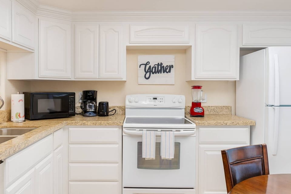 Cozy "Gather" Kitchen Haven
Bright white cabinetry, granite counters, stainless appliances, and ample storage define this inviting kitchen. Fridge, stovetop, microwave, and coffee maker ready for meals; "Gather" sign sets warm hosting vibe.