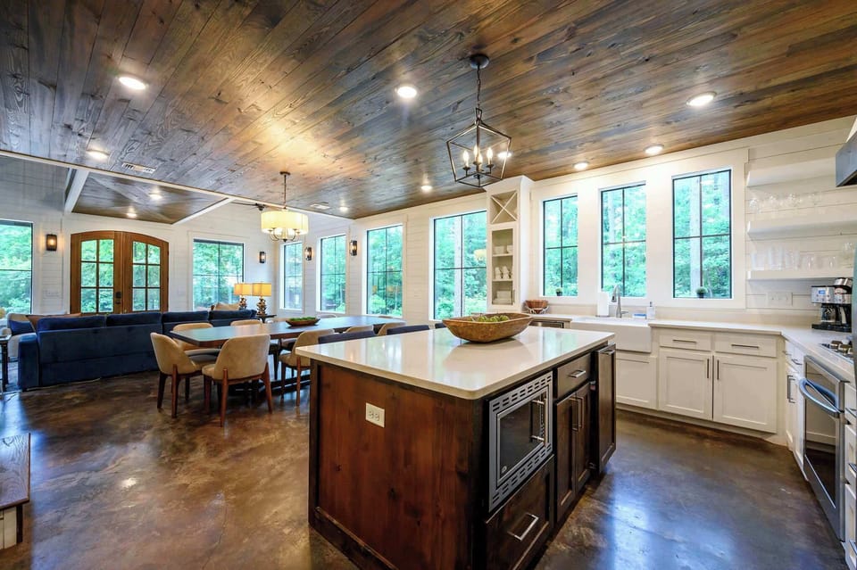 Wide open and made for groups — this kitchen-to-dining flow under a reclaimed wood ceiling is where cabin life happens.