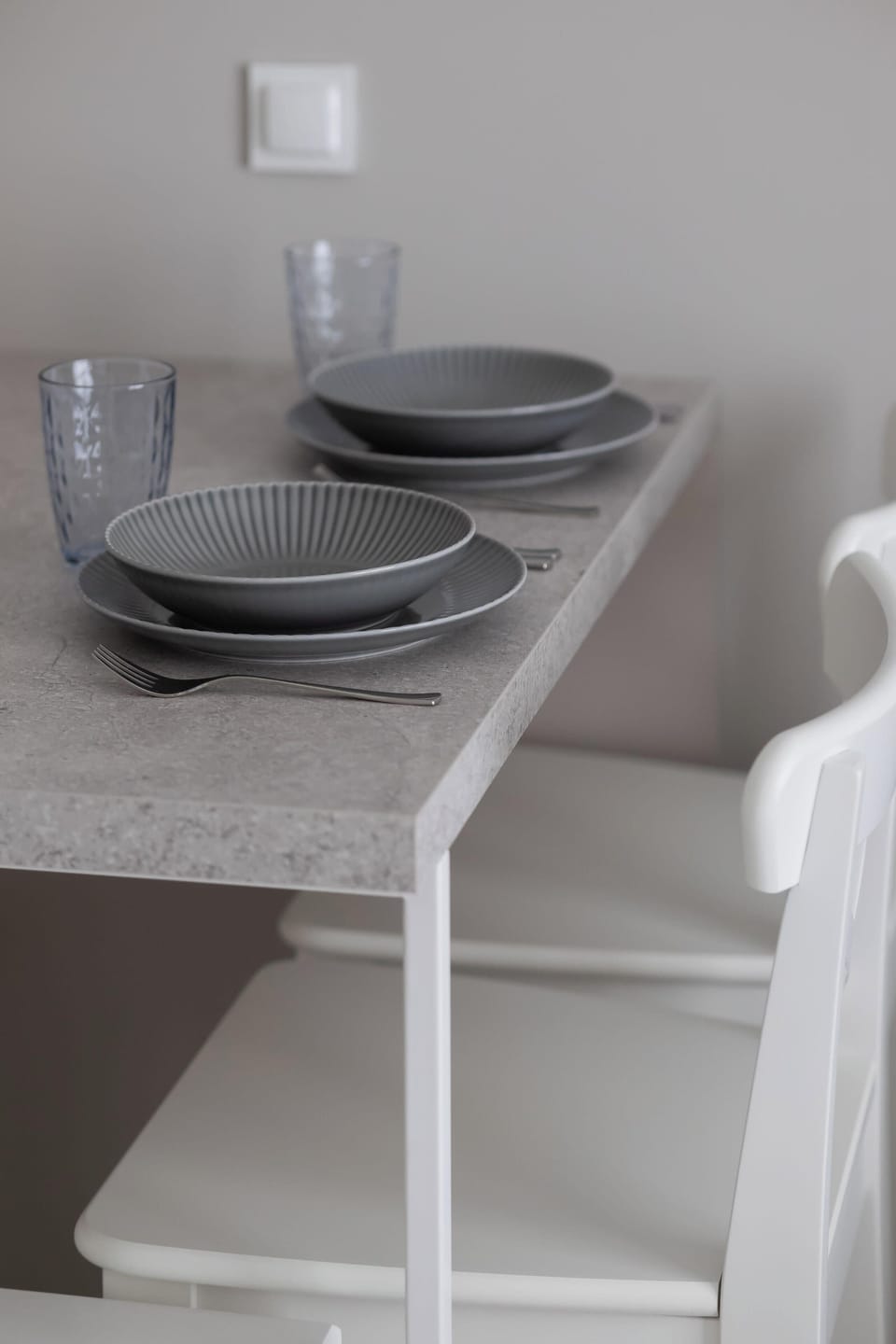 A close-up of a dining table set with plates and bowls. Simple tableware matches the minimalist interior style. The setup feels practical and elegant.