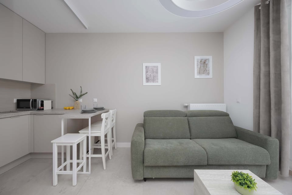 A living area with a green sofa and a small dining table beside it. White walls and minimalist décor keep the room feeling open. The layout is compact and functional.