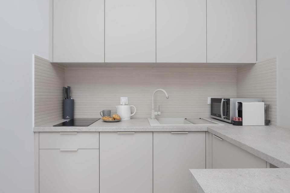 A kitchen view with white cabinetry, a kettle, and clean countertops. The appliances are neatly arranged. The design emphasizes simplicity.