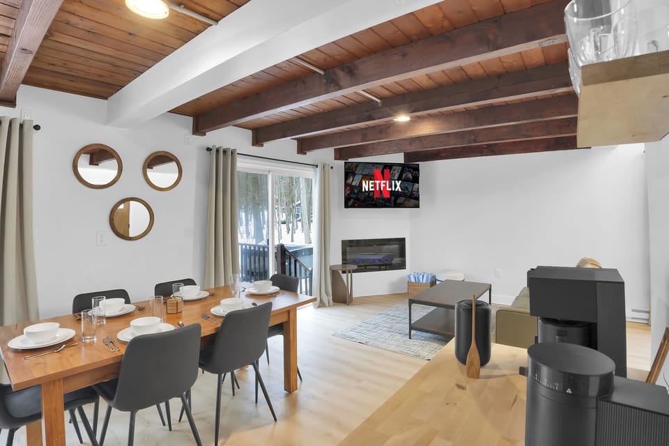 The electric fireplace anchors the open living space, adding warmth and ambiance beneath exposed wood beams. Framed by comfortable seating and natural light, it’s a cozy focal point for relaxing and gathering.