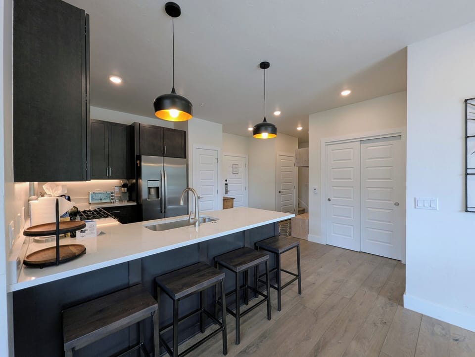 Gather around this sleek kitchen island with stylish pendant lighting overhead. Modern dark cabinetry, stainless appliances, and bright countertops create your perfect space for cooking and conversation.