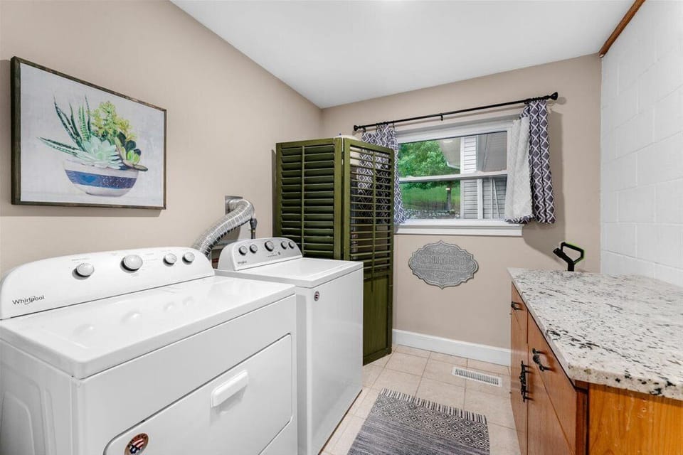 A functional laundry area with a white washer and dryer, countertop, and window.
