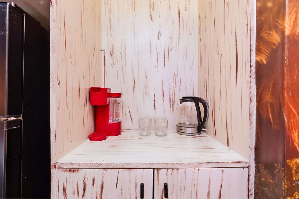 Compact kitchen corner with a red coffee maker, electric kettle, and two glasses on a rustic white wooden shelf.