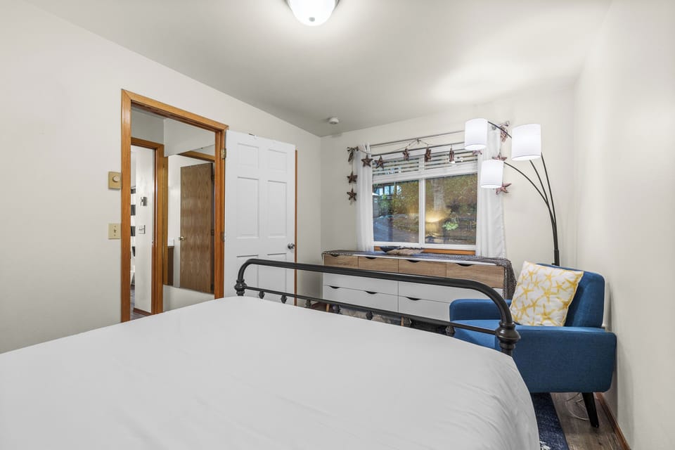 Bedroom with white walls, a white bed, and a small blue chair near the window.