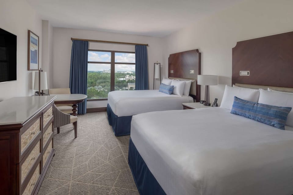 Two queen beds with soft blue accents and window view of greenery