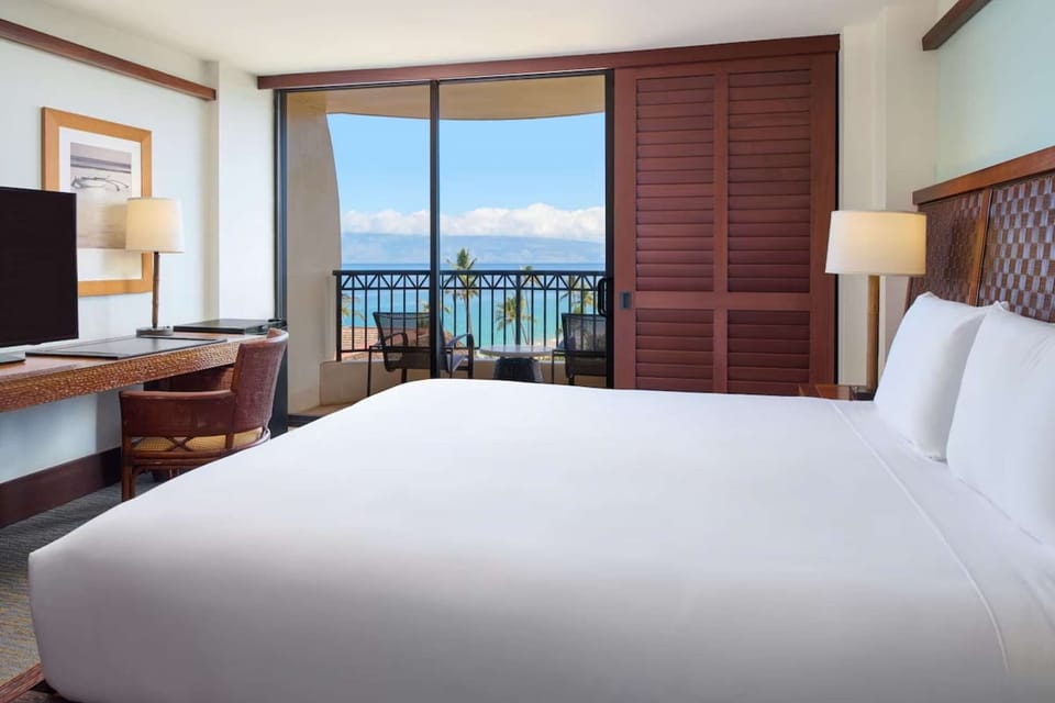 Ocean-view room with king bed, balcony seating, desk, and TV setup