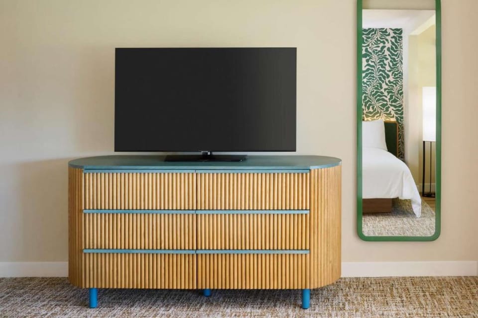 Flat-screen TV on dresser next to mirror reflecting cozy bedroom