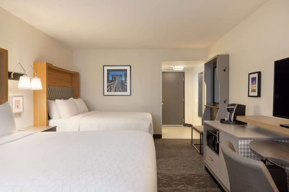 Room with two queen beds, work desk, TV, and coffee maker near entry
