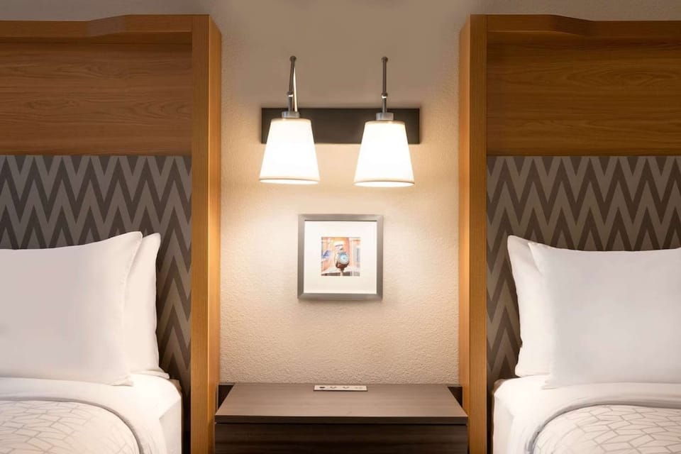 Two queen beds with shared nightstand and soft overhead lighting