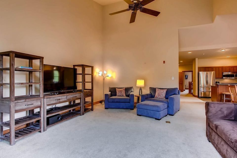 The inviting atmosphere features plush seating arranged around a contemporary entertainment center and a glimpse of the kitchen beyond.