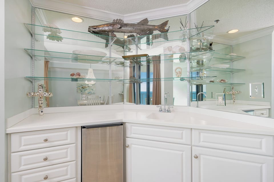Explore the refreshing wet bar with mirrored shelves reflecting coastal decor and cool beverages