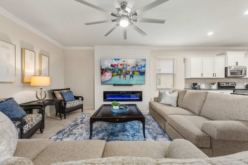 Relax on two sofas in the open living area featuring an electric fireplace, shiplap accent wall, 84" smart TV, Bluetooth soundbar, and oversized ceiling fan.