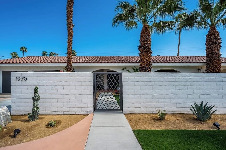 Bright exterior — gated entry, white block privacy wall, desert landscaping, and terracotta roof — exactly the mid-century curb appeal you booked