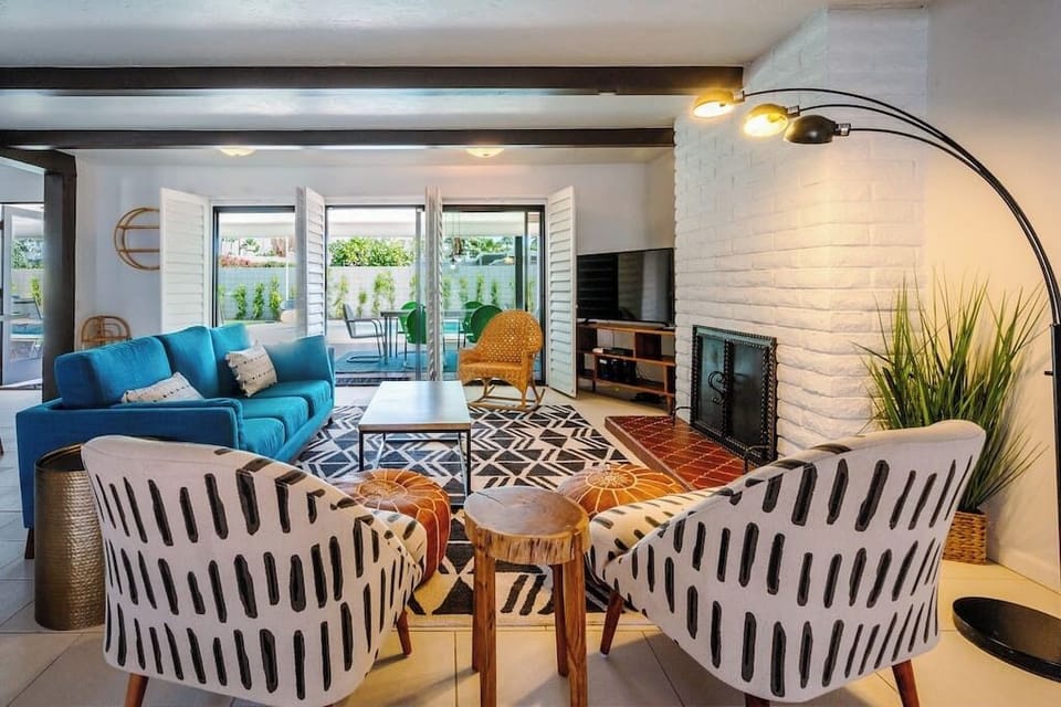 Bright mid-century living room with white brick fireplace, exposed beam ceiling, and pool-view sliding doors — indoor-outdoor Palm Springs at its best