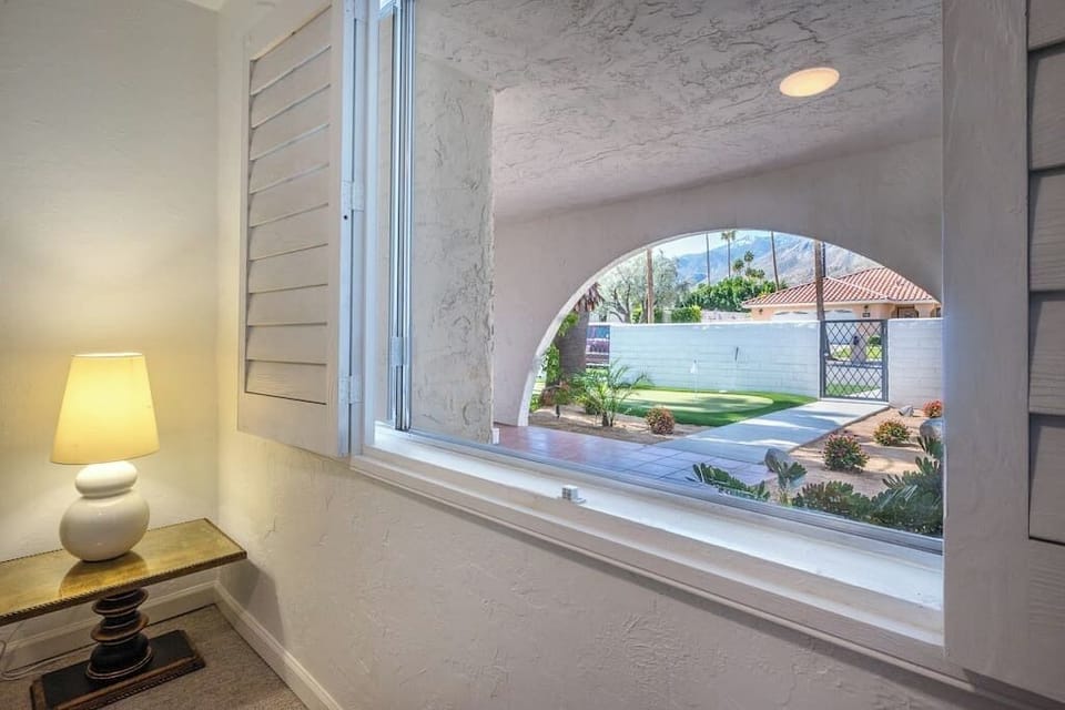 Interior hallway with arched window framing the putting green and mountain backdrop — Palm Springs charm at every turn