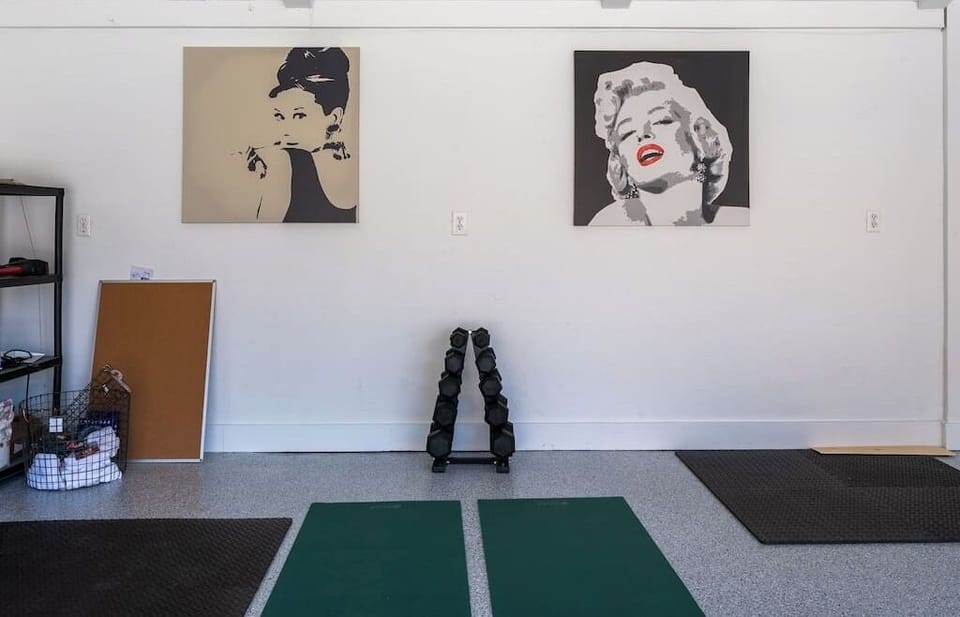 Garage space with dumbbell rack, yoga mats, and pop-art murals — Audrey and Marilyn watching over your reps
