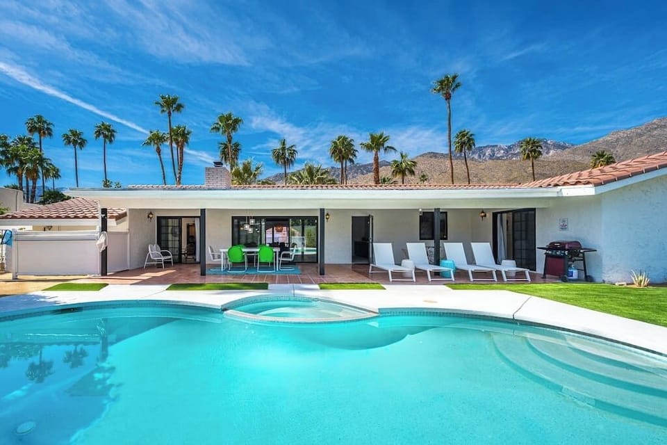 Bright pool and hot tub with mountain backdrop, sun loungers, outdoor dining, and gas grill — the backyard that seals the booking