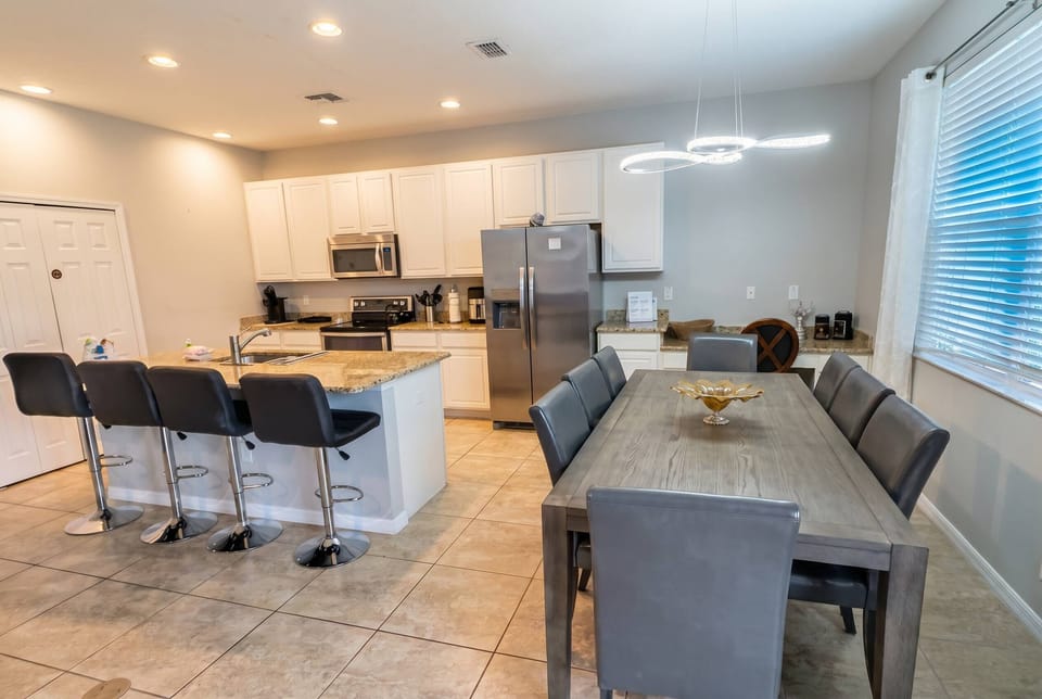 This bright, modern kitchen boasts sleek stainless steel appliances and a spacious island with stylish bar seating, ideal for casual gatherings, while the inviting dining area is perfect for shared meals and joyful moments.