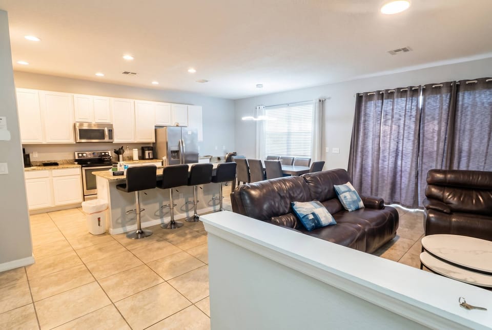 Experience the perfect blend of a sleek kitchen and cozy living area, highlighted by warm tile floors and modern furnishings, as natural light pours through stylish curtains, making it an ideal retreat after your adventures.