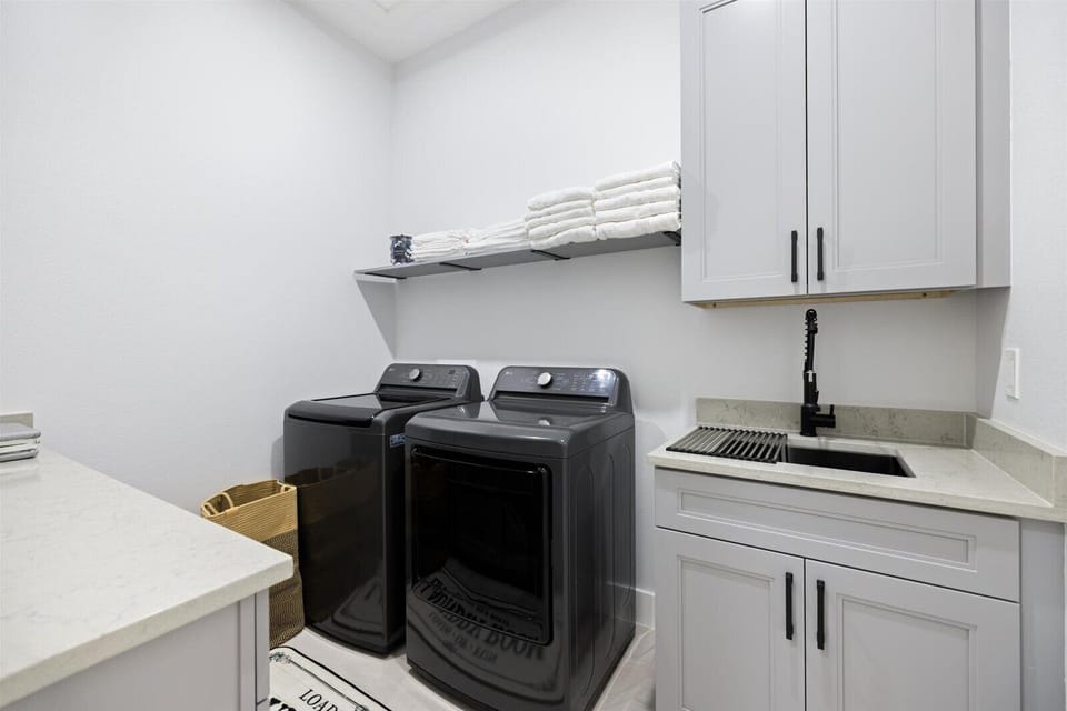 Laundry room with dryer, utility sink, iron, and ironing board.
