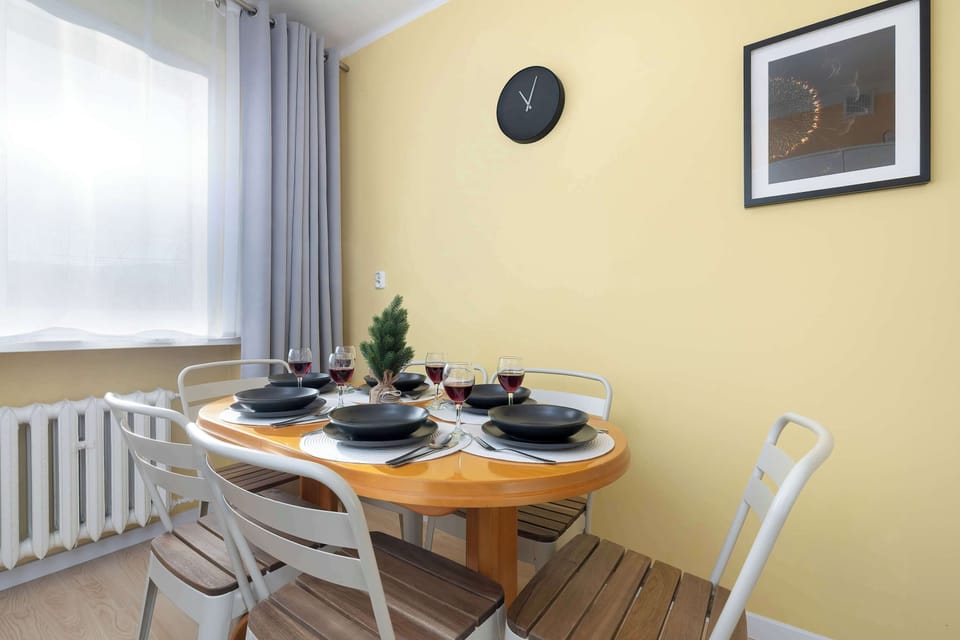 A dining area with a round wooden table and white chairs. Table settings are neatly arranged. The yellow walls create a cheerful atmosphere.