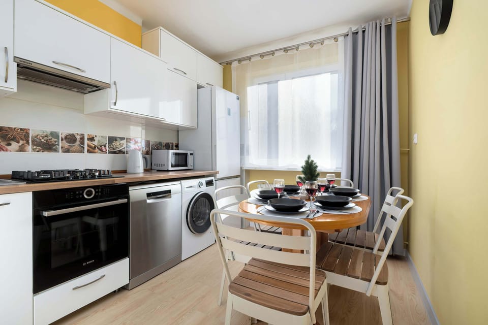 A compact kitchen with white cabinets, a stove, and a washing machine. Wooden countertops add warmth to the design. The layout is practical and efficient.
