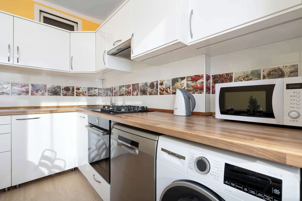 A closer kitchen angle highlighting the stove, microwave, and washing machine. Shelves above the counter provide extra storage. The design is compact but complete.