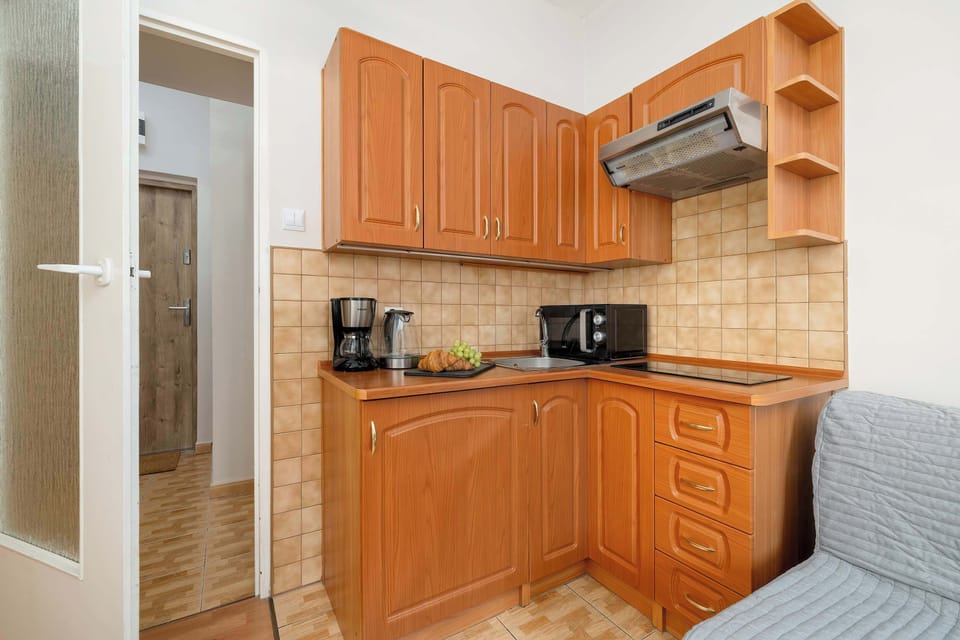 A narrow kitchen corridor with wooden cabinetry, tiled walls, and a bed partially visible at the edge of the frame.