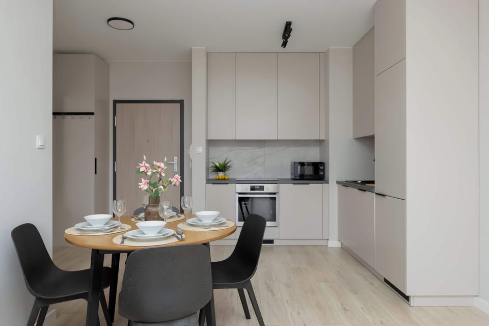 A wider dining and kitchen view with white cabinetry and modern appliances. The space feels open and uncluttered. Light finishes give it a fresh appearance.