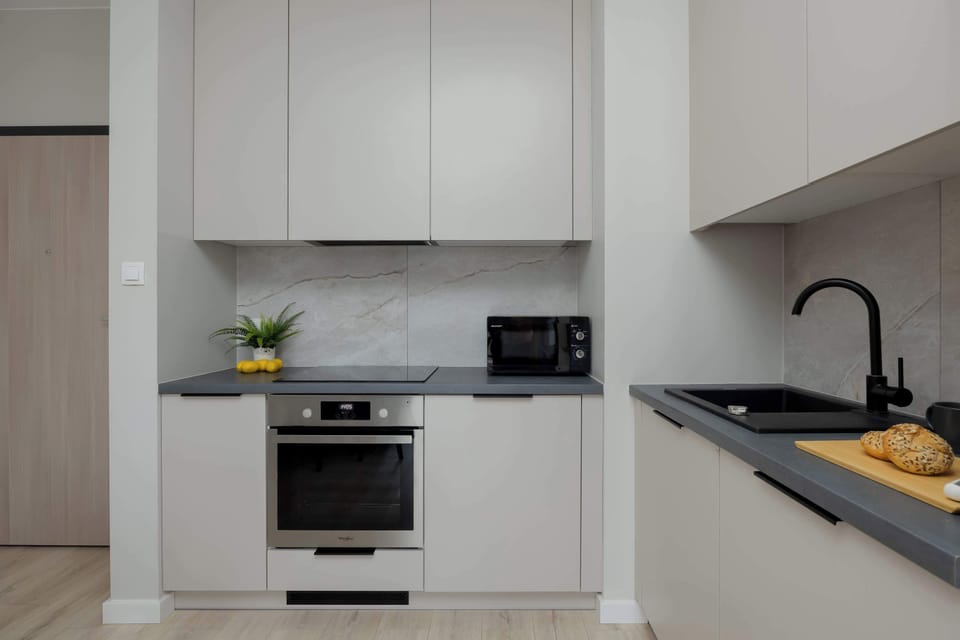 A compact kitchen with white cabinets, built-in oven, and microwave. The countertops are clean and uncluttered. The design is minimal and modern.