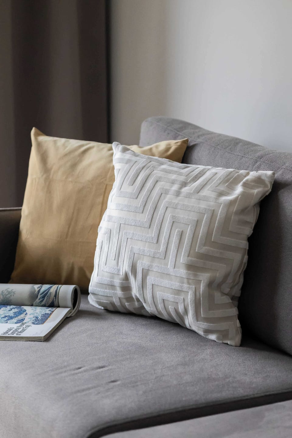 A close-up of decorative pillows arranged on a gray sofa. Soft textures and neutral tones create a comfortable feel. The styling looks clean and inviting.