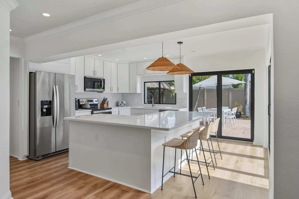 Modern white kitchen with island, stainless steel appliances, pool view