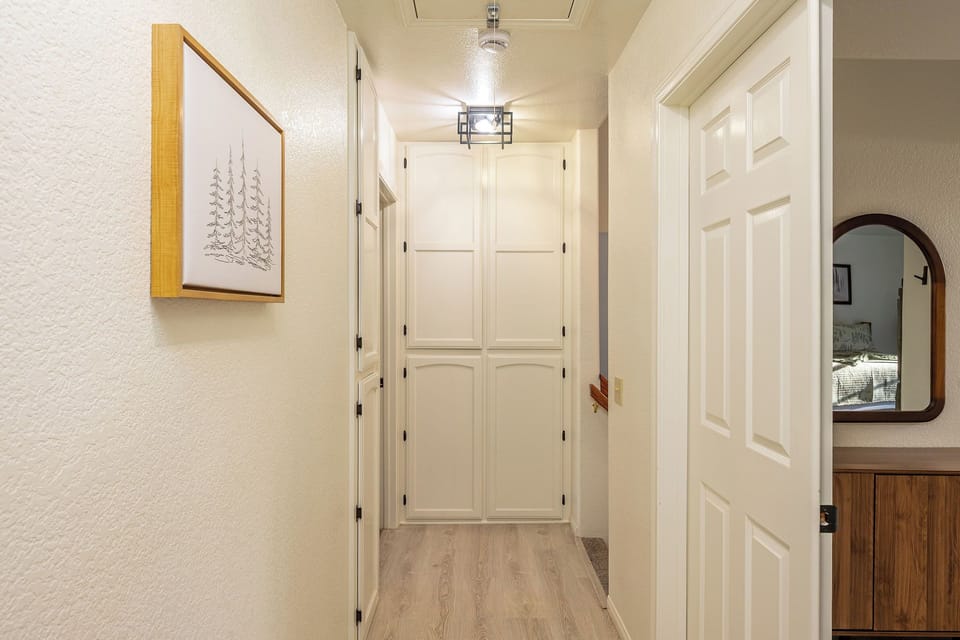 Upstairs hallway featuring clean white doors, warm lighting, and thoughtful touches like lake artwork that create a welcoming first impression.