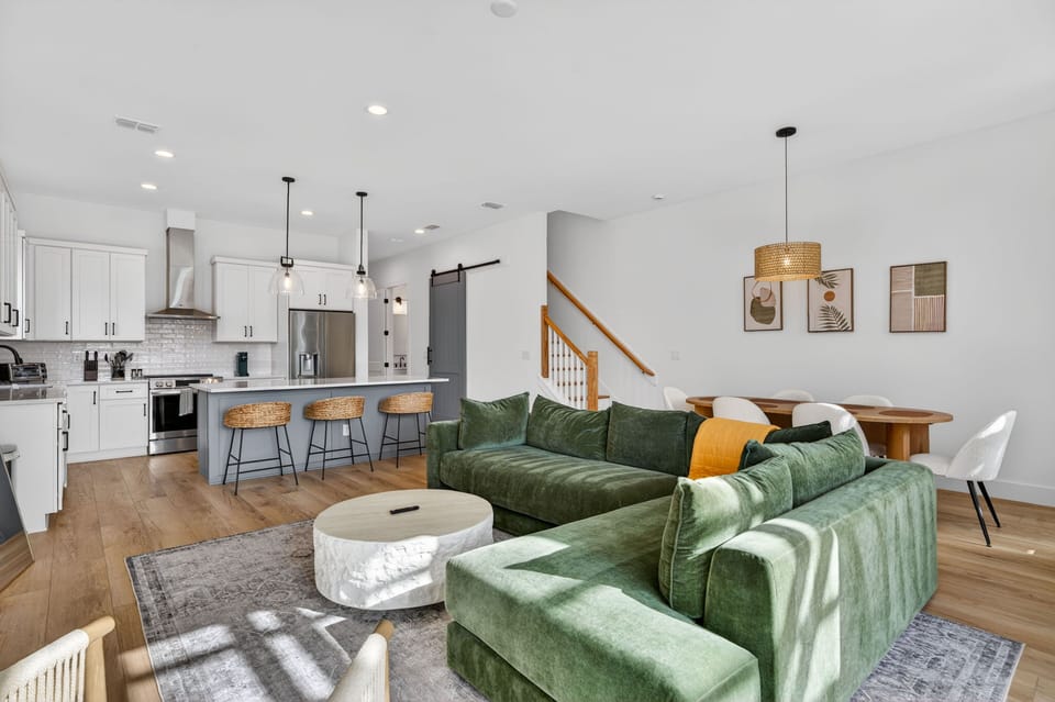 This open-concept living area showcases a cozy green sectional, seamlessly connecting to a fully equipped kitchen, ideal for family entertaining.