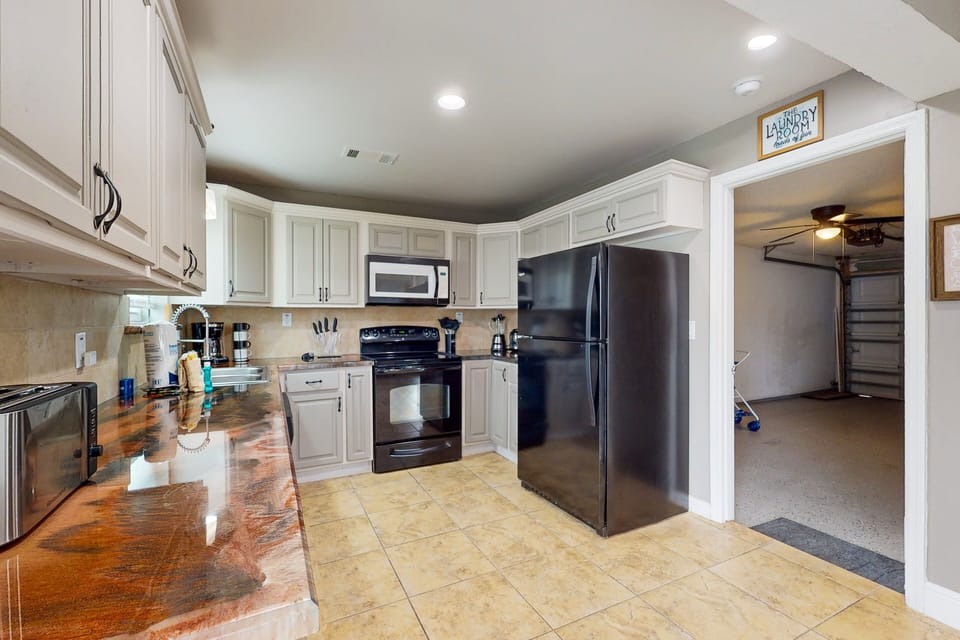 The kitchen features black themed appliances: fridge, stove, oven, microwave, dishwasher, coffee maker, and blender with full cooking utensils and dishware.