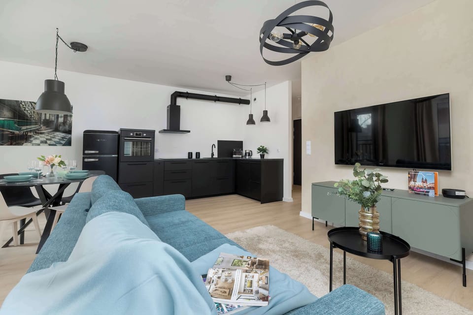 An open-plan living room with a blue sofa, TV unit, and dining area in the background. Decorative elements add warmth. The layout is practical and well-organized.
