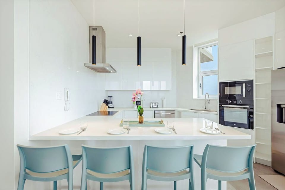 Your sleek, modern kitchen awaits with pristine white cabinetry, gleaming countertops, and a spacious island perfect for casual meals or morning coffee together.