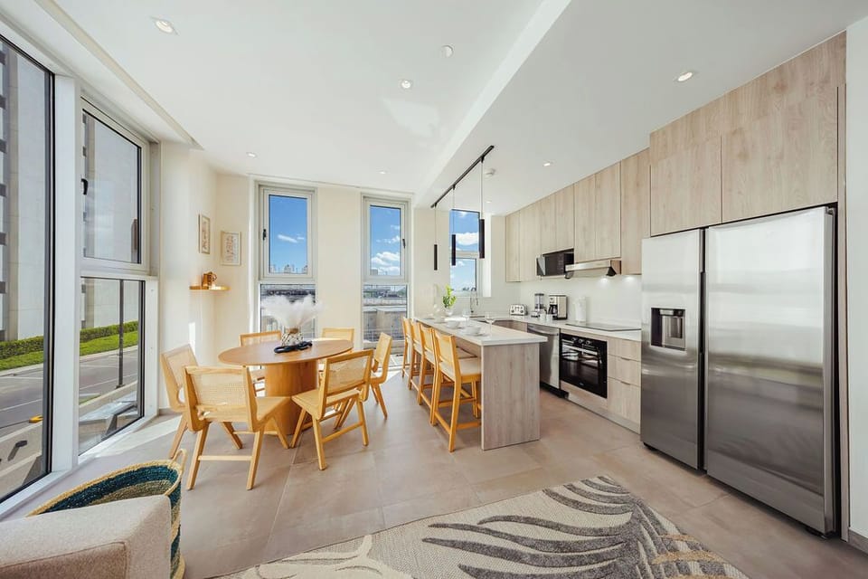 Step into your sun-filled kitchen and dining space, where modern appliances meet warm wood tones. Large windows frame the view, while your island invites morning coffee and shared meals.