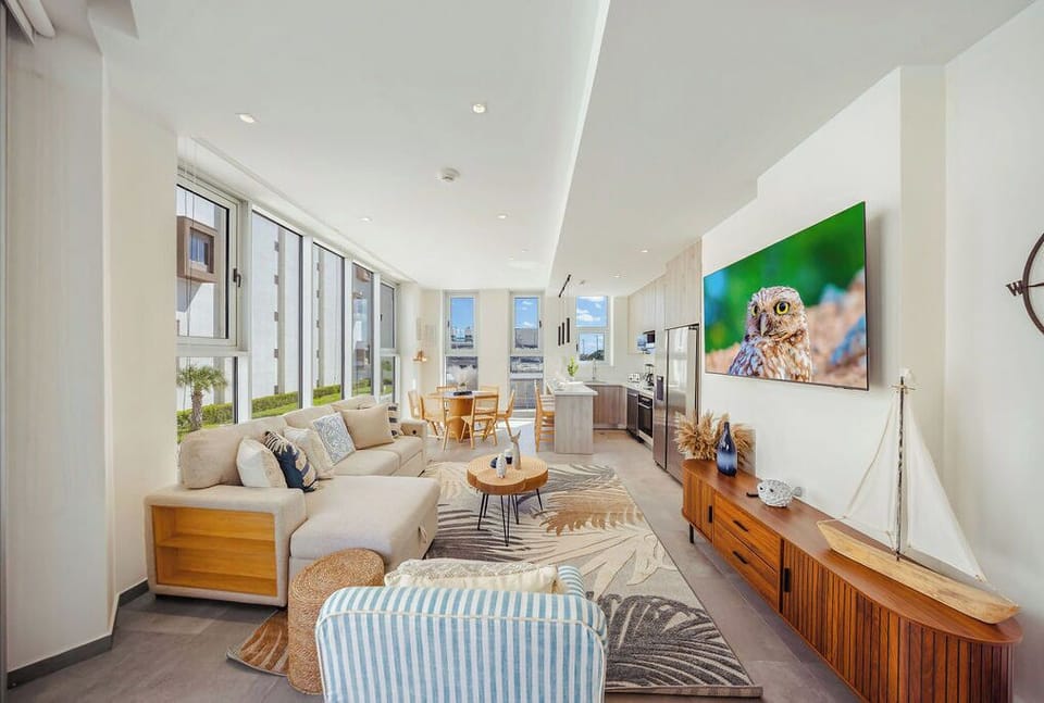 This open-concept living space invites you to unwind in coastal-inspired comfort. Floor-to-ceiling windows flood the room with natural light, while nautical touches and plush seating create your perfect retreat.