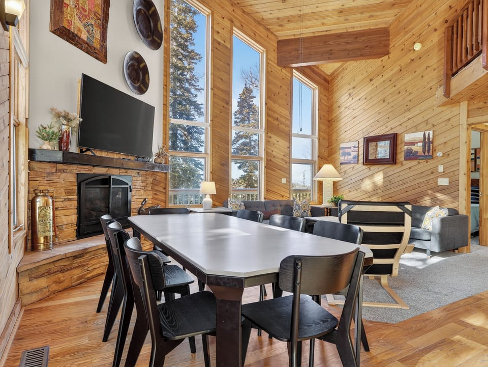 Gather around your spacious dining table with soaring ceilings, cozy fireplace, and mountain views through floor-to-ceiling windows in this warm log cabin retreat.