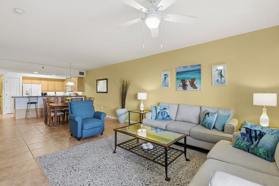 Your spacious living room flows seamlessly into the kitchen, where ocean-themed touches and cooling ceiling fan create your perfect coastal retreat.