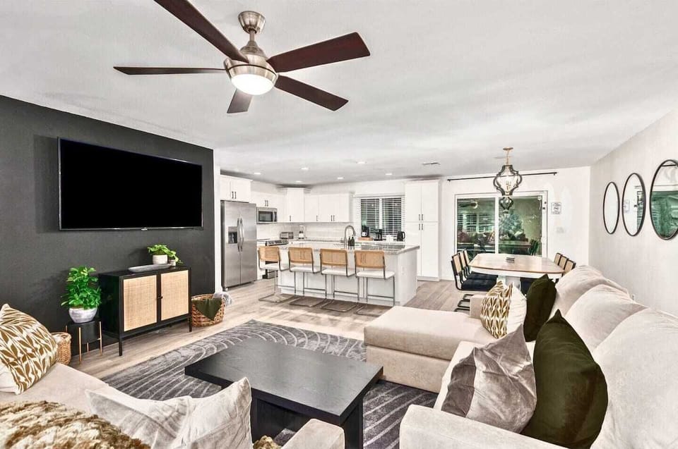 Living room with large TV, comfortable seating. You can see the dining table and part of the kitchen also