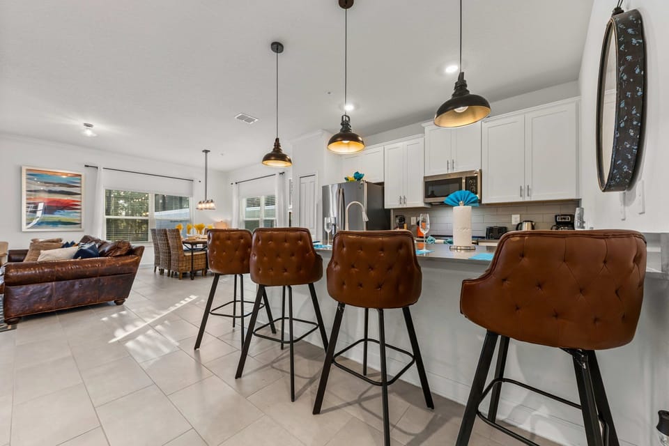 Bright, open-concept living! The stylish kitchen island with pendant lights and tufted leather stools seats four and flows seamlessly to the dining and lounge areas.